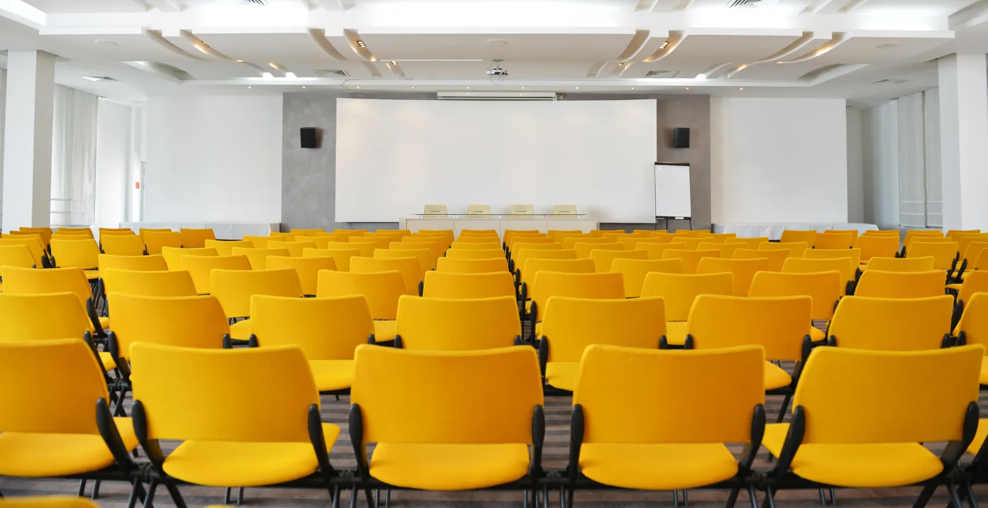 Sala conferenze con sedie gialle e sul fondo uno schermo da proiezione
