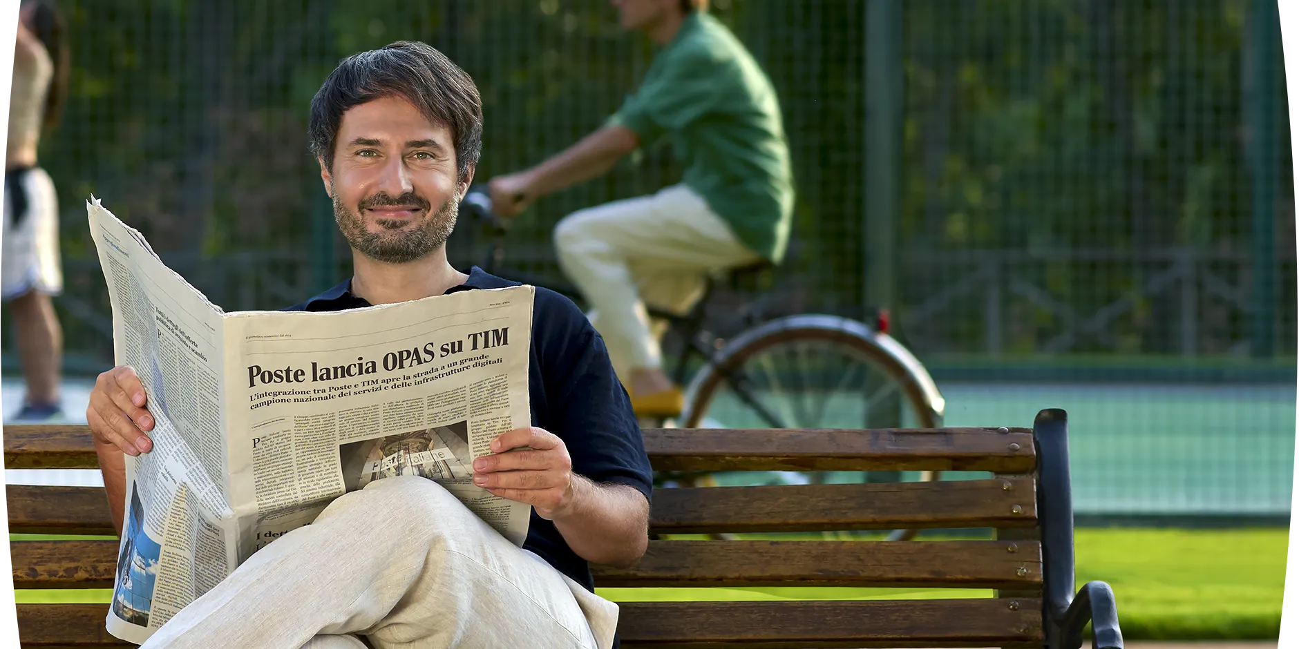 un uomo legge giornale su una panchina al parco