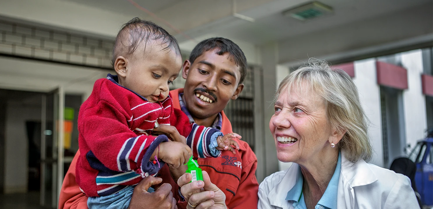 medico che sorride a un bambino tenuto in braccio da un operatore sanitario